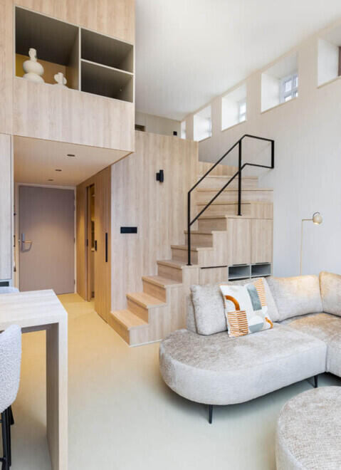 Modern interieur van een studio met houten trapkast, vide en een beige hoekbank.