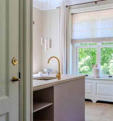 Luxe moderne keuken met kookeiland, gouden kraan en stijlvolle hanglampen bij een groot raam.