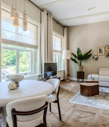 Lichte, moderne woonkamer met ronde eettafel, houten visgraatvloer en stijlvolle zithoek bij het raam.