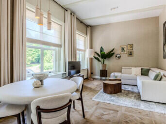 Lichte, moderne woonkamer met ronde eettafel, hoekbank en stijlvolle houten visgraatvloer.